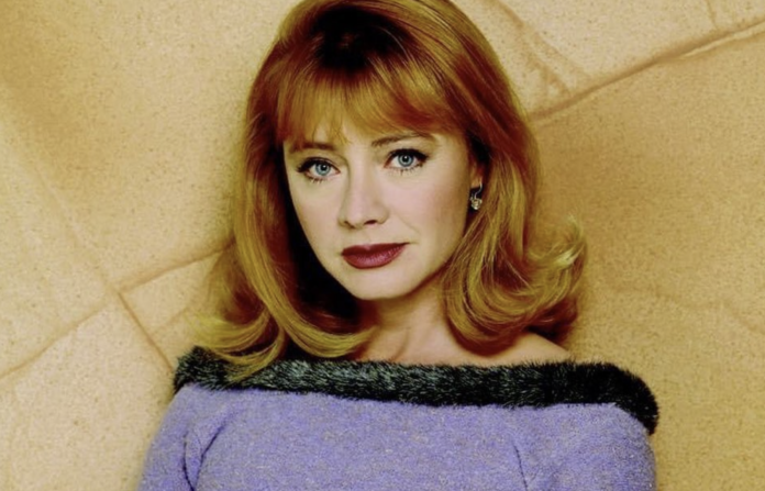 A woman with red hair and green eyes wearing a purple top with black trim. A woman with red hair and green eyes wearing a purple top with black trim.