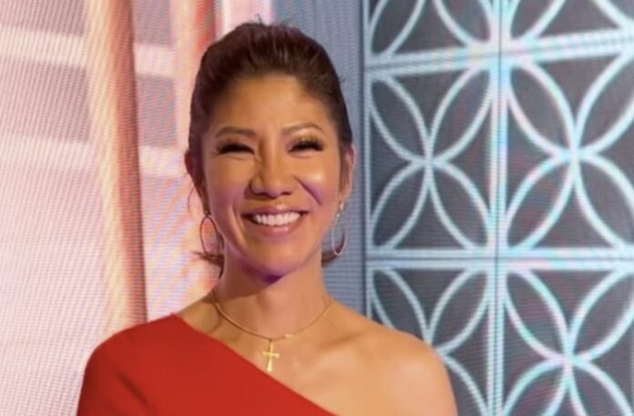 A smiling woman in a red one-shoulder dress with a patterned background. A smiling woman in a red one-shoulder dress with a patterned background.
