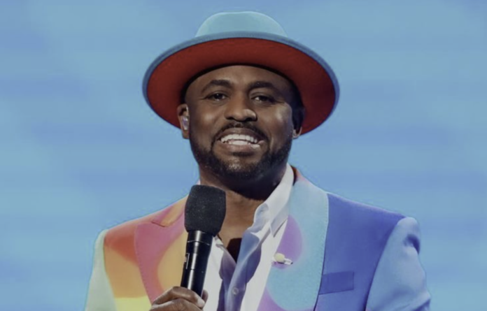 A man in a colorful jacket and hat speaking into a microphone. A man in a colorful jacket and hat speaking into a microphone.