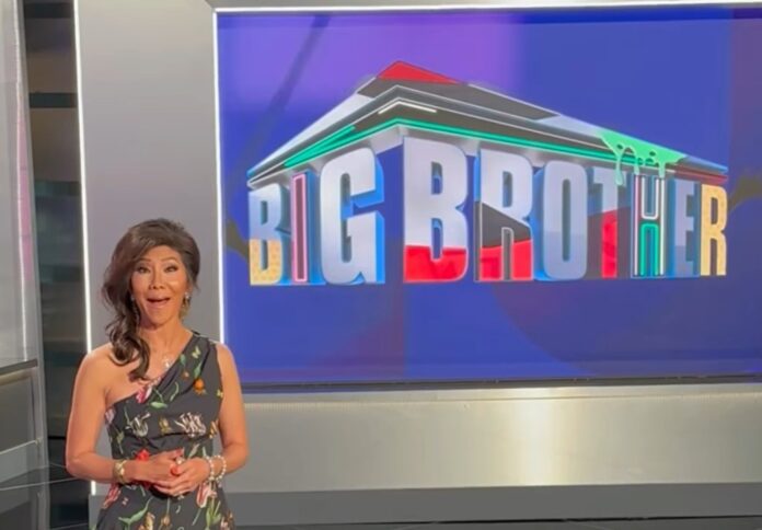A TV presenter stands beside a screen displaying the Big Brother logo. A TV presenter stands beside a screen displaying the Big Brother logo.