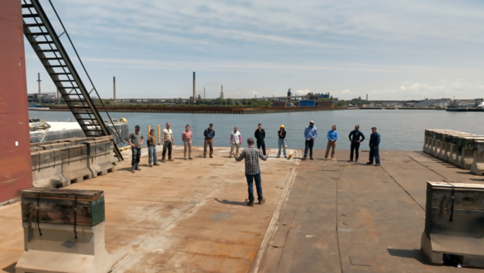 Man addressing a group of people on a dock near an industrial waterfront. Man addressing a group of people on a dock near an industrial waterfront.