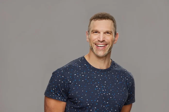 Smiling man in a speckled navy blue t-shirt against a gray background. Smiling man in a speckled navy blue t-shirt against a gray background.