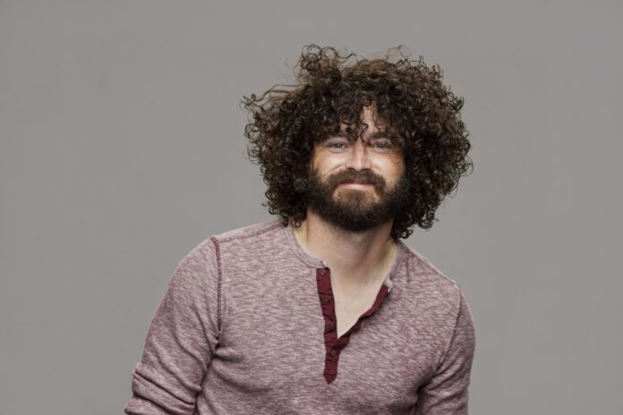 A man with curly hair and beard wearing a maroon henley shirt. A man with curly hair and beard wearing a maroon henley shirt.