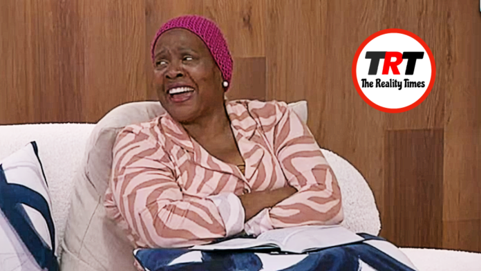 A joyful woman in a pink headscarf and patterned jacket smiles warmly while sitting indoors. A joyful woman in a pink headscarf and patterned jacket smiles warmly while sitting indoors.