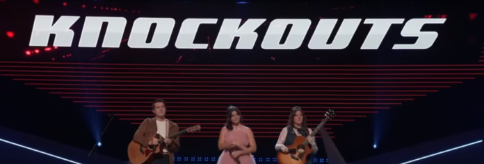 Three women performing on stage with musical instruments under 'Knockout' sign. Three women performing on stage with musical instruments under 'Knockout' sign.