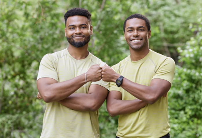 Two men smiling and bumping fists outdoors, wearing matching beige shirts. Two men smiling and bumping fists outdoors, wearing matching beige shirts.