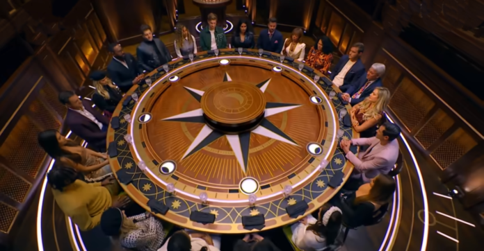 People gathered around a large, ornate round table with a compass design. People gathered around a large, ornate round table with a compass design.