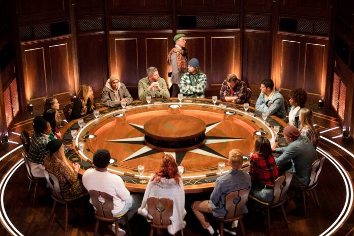 People gathered around a large round table in a warmly lit room. People gathered around a large round table in a warmly lit room.