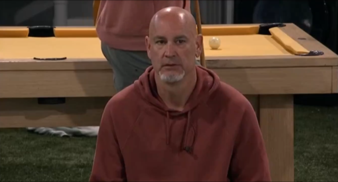 A bald man in a brown hoodie sitting indoors. A bald man in a brown hoodie sitting indoors.