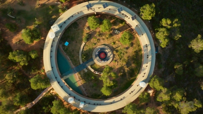 Aerial view of a circular structure with a central tower and surrounding greenery. Aerial view of a circular structure with a central tower and surrounding greenery.