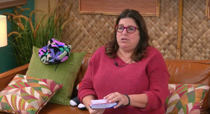 A woman wearing glasses and a red sweater is sitting on a green couch, holding papers. A woman wearing glasses and a red sweater is sitting on a green couch, holding papers.