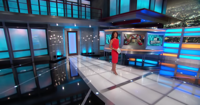 A news anchor stands in a modern, brightly lit TV studio. A news anchor stands in a modern, brightly lit TV studio.