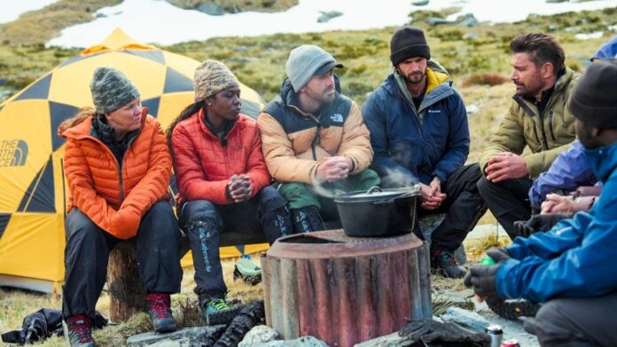 Group of friends camping outdoors, warming by a pot on a fire. Group of friends camping outdoors, warming by a pot on a fire.