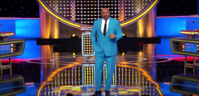 Steve Harvey in a bright blue suit on a game show stage. Steve Harvey in a bright blue suit on a game show stage.