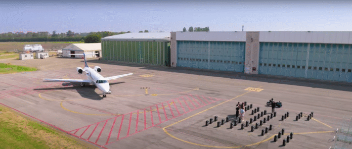 A crowd gathered near an airplane at an airport hangar on a clear day. A crowd gathered near an airplane at an airport hangar on a clear day.