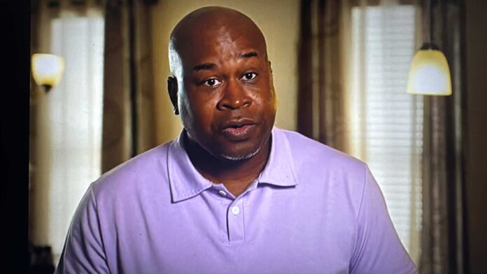 Man in a purple polo shirt speaking indoors. Man in a purple polo shirt speaking indoors.