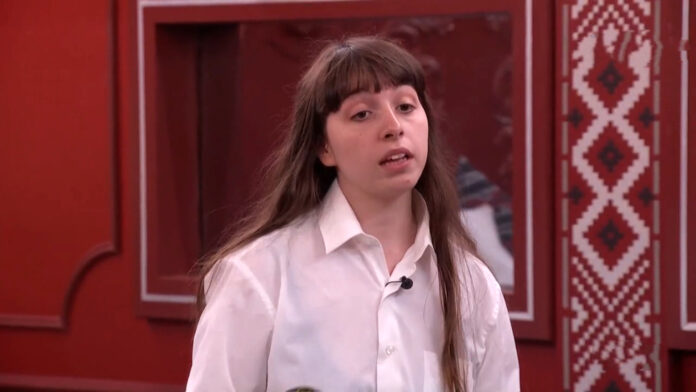 A young woman with long hair wearing a white shirt stands indoors. A young woman with long hair wearing a white shirt stands indoors.