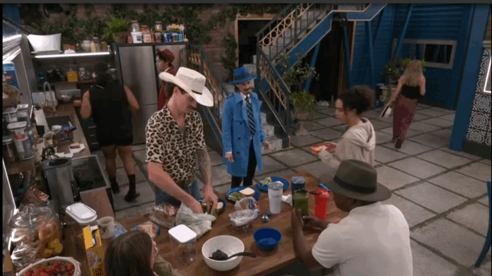 People gathered around a table with food and drinks, one wearing a cowboy hat. People gathered around a table with food and drinks, one wearing a cowboy hat.