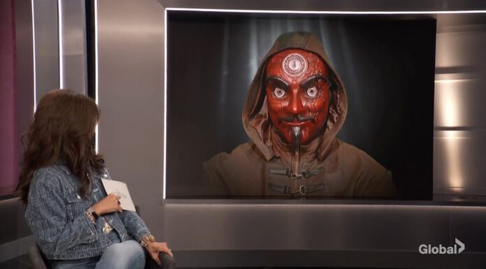 A person sits in an art gallery viewing a striking portrait of a red-faced figure with three eyes. A person sits in an art gallery viewing a striking portrait of a red-faced figure with three eyes.