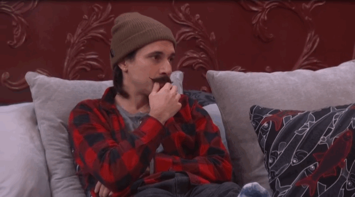 Man in a brown beanie and red plaid shirt eating a cupcake on a couch. Man in a brown beanie and red plaid shirt eating a cupcake on a couch.