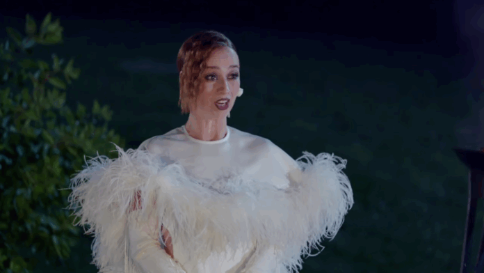 A woman in a white feathered outfit gestures dramatically in the dark. A woman in a white feathered outfit gestures dramatically in the dark.
