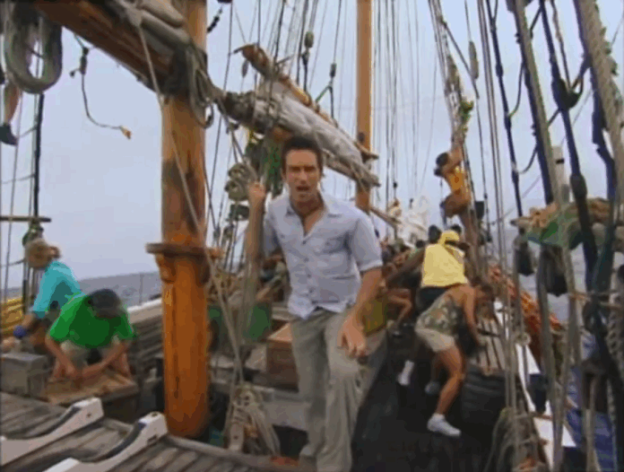 Man standing on a wooden sailboat deck among ropes and sails. Man standing on a wooden sailboat deck among ropes and sails.