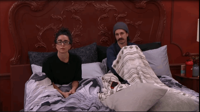 Two people sitting on a bed under blankets, looking forward. Two people sitting on a bed under blankets, looking forward.