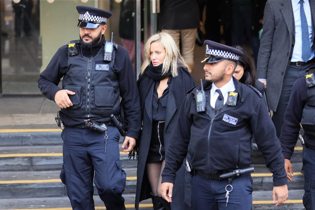 Two police officers escort a woman in black clothing.